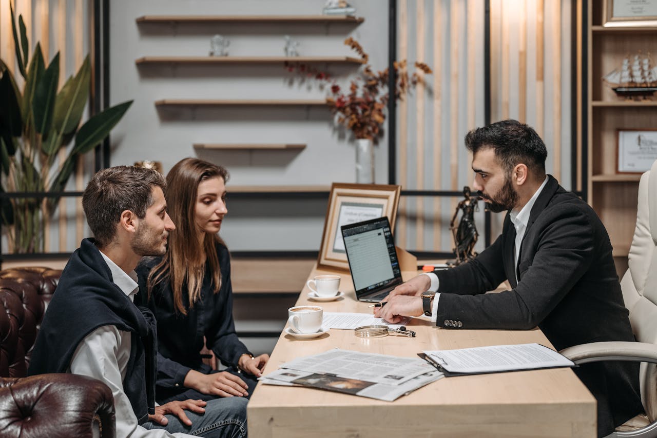 why-choose-us Three professionals engaged in a business discussion at an office desk with a laptop.