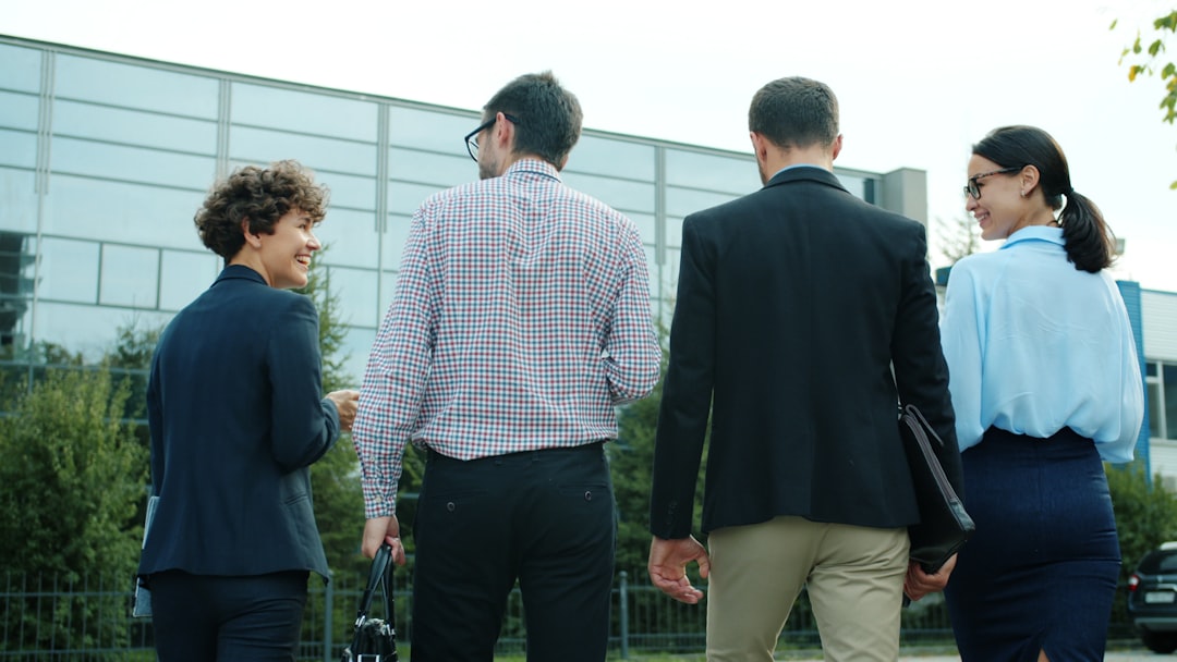 Back view of group of young businesspeople men and women walking to office center talking discussing business. Young ambitious people and city lifestyle concept.